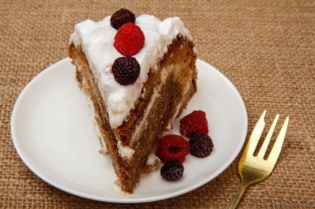 Fetta di torta di biscotti fatta in casa decorata con panna montata e lamponi sul tavolo con tela di sacco