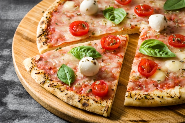 Fetta italiana della pizza con i pomodori, il formaggio e il basilico sulla fine nera della pietra su