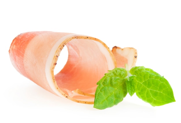 Fetta rotolata di prosciutto isolata vicino alle foglie del basilico