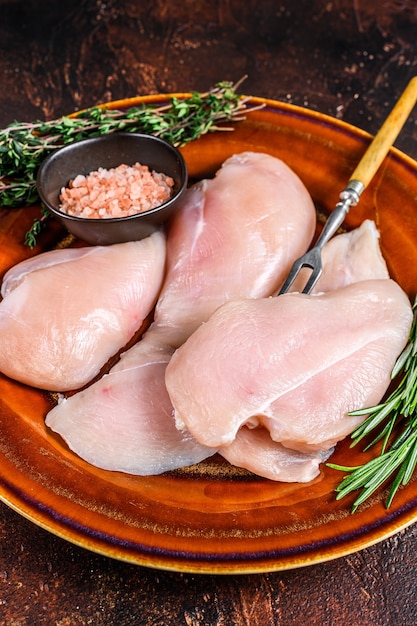 Fette crude di filetto di petto di pollo su un piatto rustico con erbe aromatiche. Sfondo scuro. Vista dall'alto.