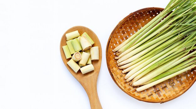 Fette della citronella sul cucchiaio di legno con citronella fresca nel canestro di trebbiatura di bambù di legno su bianco isolato. Copia spazio