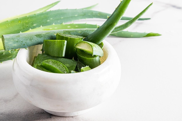 Fette di aloe vera succosa fresca in un mortaio di marmo bianco per la preparazione di un rimedio naturale cosmetico in primo piano a casa