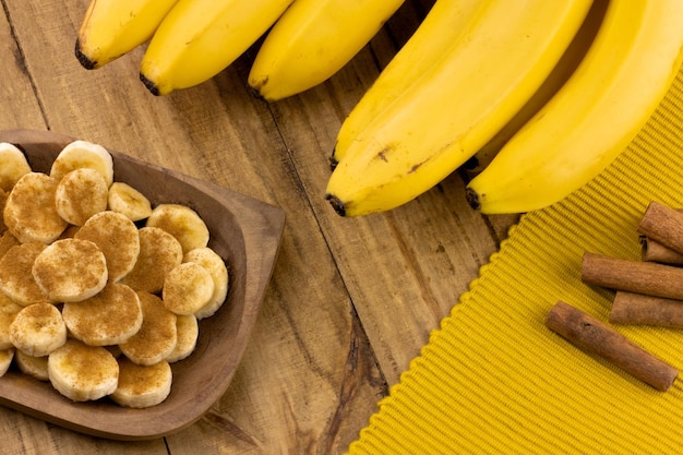 Fette di banana con bastoncini di cannella alla cannella e mazzo di banane sul tavolo in legno vista dall'alto