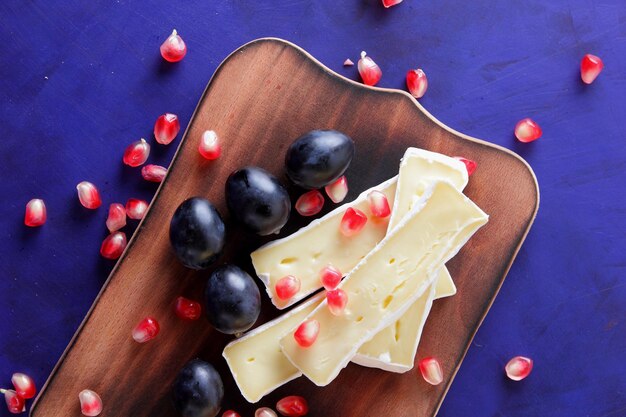 Fette di camembert con semi di melograno uva scura e noci su sfondo blu Delizioso formaggio su una tavola di legno alzato