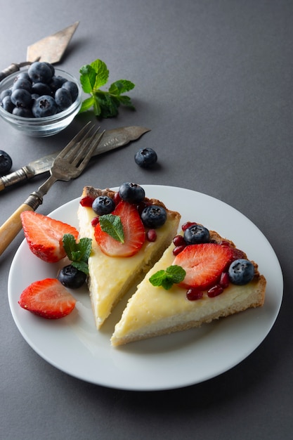 Fette di cheesecake con frutti di bosco freschi e menta per dessert. Sfondo grigio