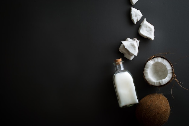 fette di cocco fresco con una bottiglia di olio di cocco spremuto a freddo su sfondo nero