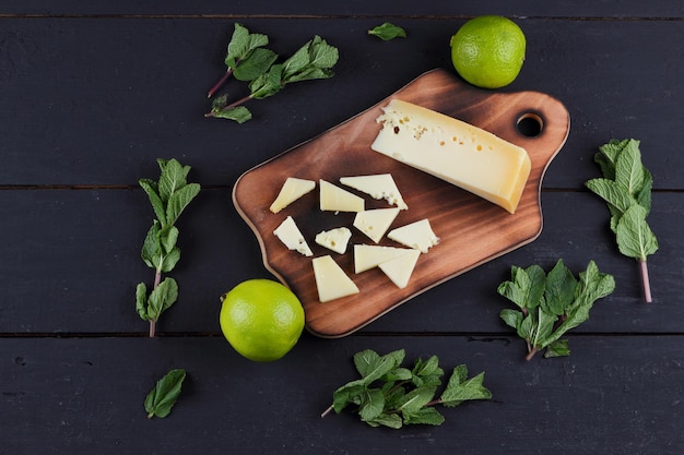 Fette di formaggio a pasta dura gialla su una tavola di legno con agrumi con menta fresca su sfondo nero in legno Primo piano di una natura morta Vista dall'alto