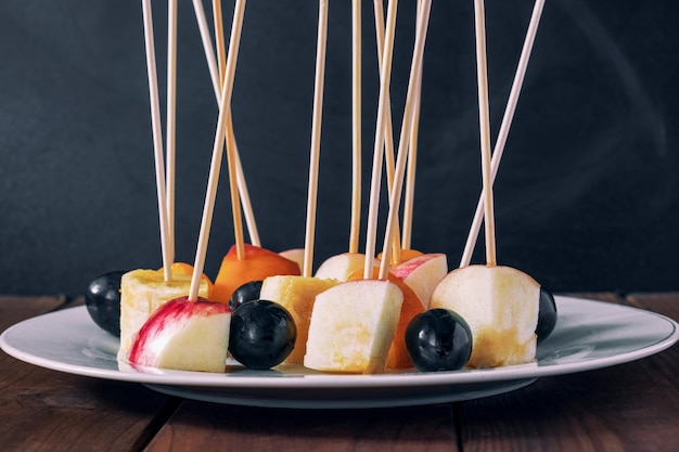 Fette di frutta infilate su un bastone di legno adagiato in un piatto bianco su uno sfondo scuro