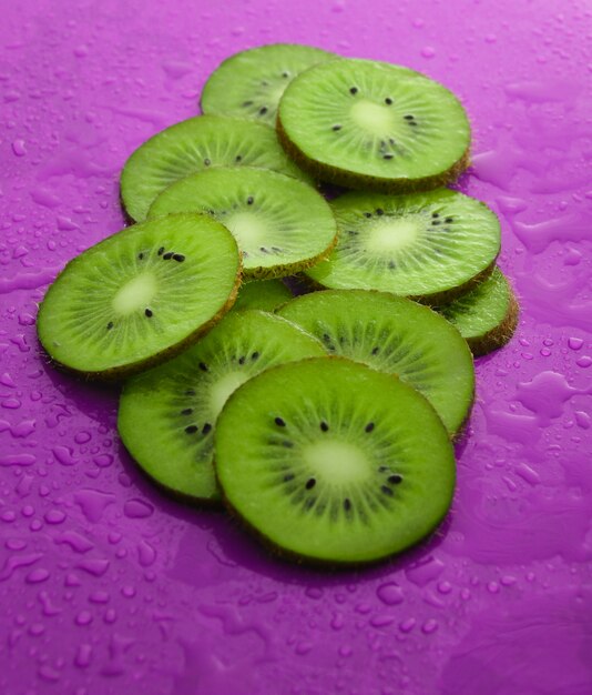 Fette di kiwi in gocce d'acqua su uno sfondo viola. Concetto di frutta.