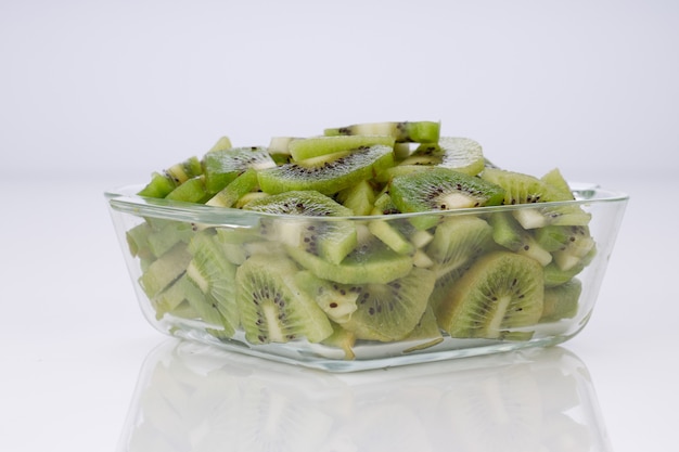 Fette di kiwi o pezzi tagliati disposti in un contenitore quadrato di vetro con sfondo di colore bianco.