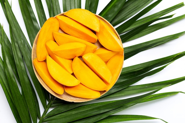 Fette di mango sul piatto di legno su foglie di palma tropicale.