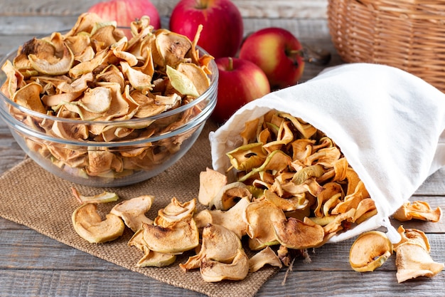 Fette di mela organiche essiccate al sole fatte in casa, chips di mele croccanti, su un vecchio tavolo in legno rustico con mela fresca. Mangiare sano. Vitamine.