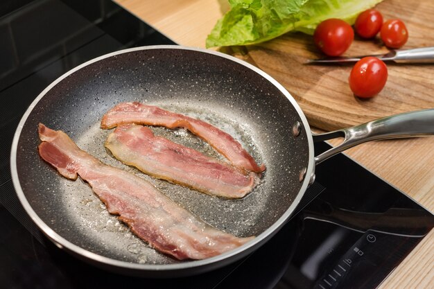 Fette di pancetta fritta fresca in padella per colazione, ingredienti per insalata caesar di pollo, cottura su vera cucina