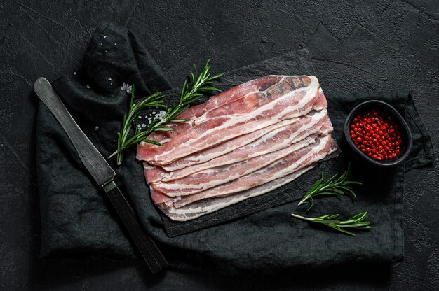 Fette di pancetta su un tagliere di pietra. Carne di maiale. Sfondo nero. Vista dall'alto