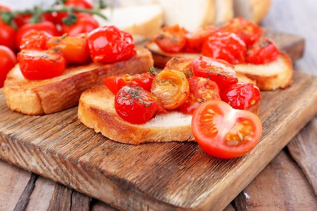 Fette di pane bianco tostato con pomodori in scatola sul tagliere sul primo piano della tavola di legno