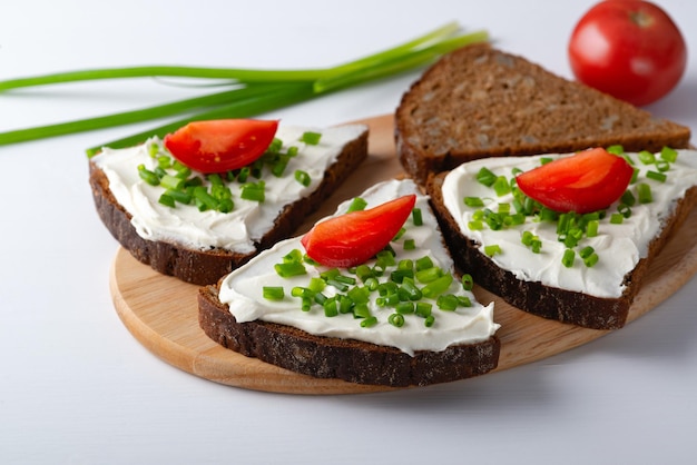 Fette di pane con la cipolla e i pomodori della ricotta sul piatto di legno su fondo bianco