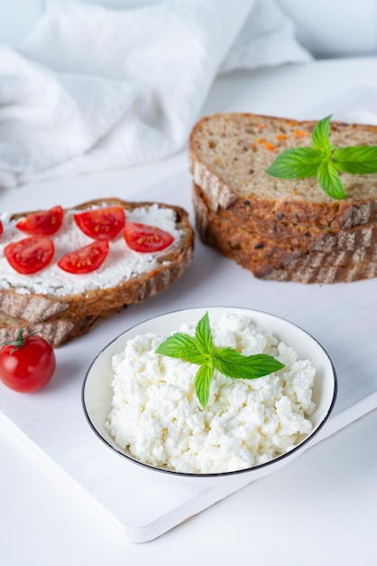 Fette di pane con ricotta e pomodorini su tagliere di legno su sfondo bianco