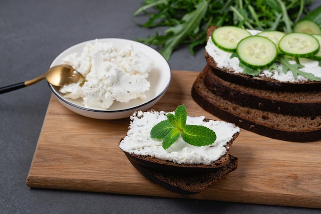 Fette di pane di segale con ricotta e cetrioli su sfondo grigio