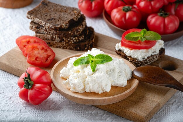 Fette di pane di segale con ricotta e pomodori sul piatto di legno su fondo bianco