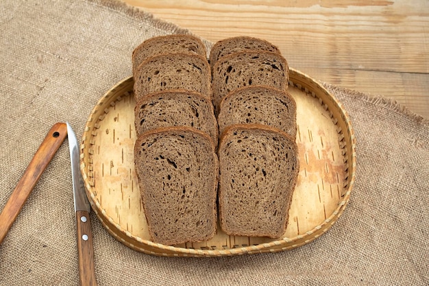 Fette di pane di segale scuro giacciono in un vassoio di legno su una tovaglia di lino Stile rurale