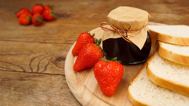 Fette di pane e delizioso vasetto di marmellata di fragole e frutti di bosco freschi su legno