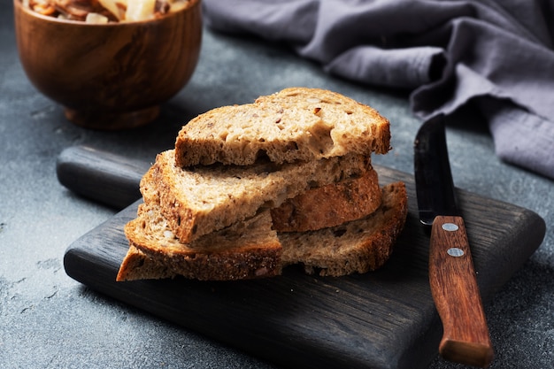 Fette di pane integrale su un tagliere di legno. Sfondo scuro di cemento.