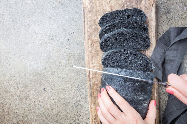 Fette di pane nero colorato al nero di seppia su grigio con mani di donna