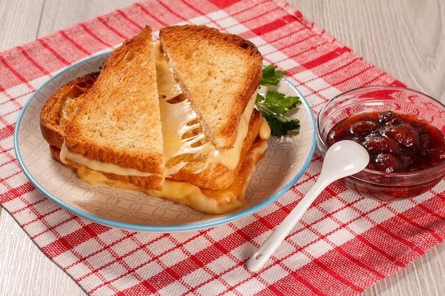 Fette di pane tostate con formaggio e prezzemolo verde su una ciotola di vetro lastra bianca con marmellata di fragole