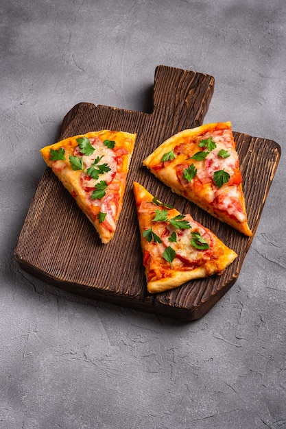 Fette di pizza calda con pomodoro prosciutto mozzarella e prezzemolo sul tagliere di legno marrone pietra cemento sfondo angolo di visione