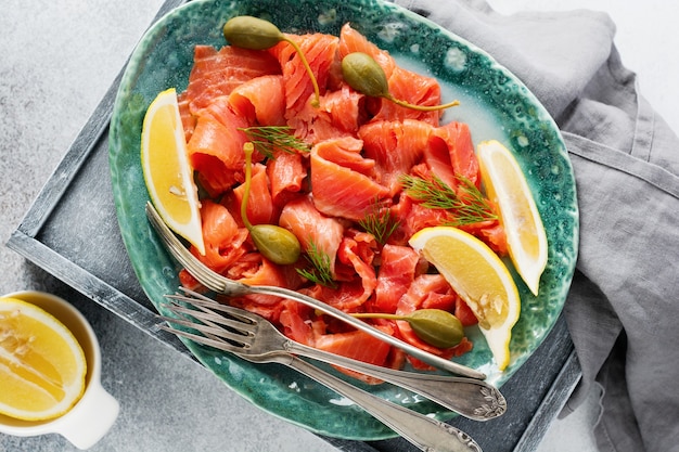 Fette di salmone leggermente salato con capperi, limone e aneto su un piatto di ceramica su un tavolo di cemento grigio. Vista dall'alto.