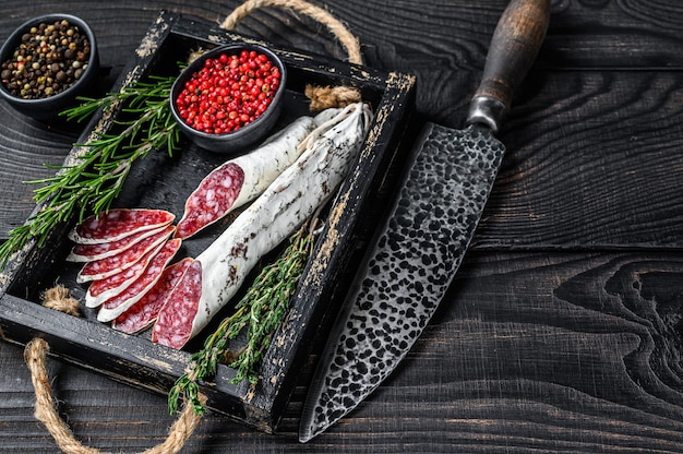 Fette di salsiccia Fuet con timo e rosmarino in una teglia di legno.