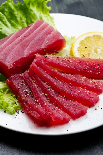 Fette di sashimi di tonno rosso crudo sul piatto bianco su backgr di legno