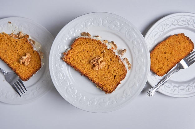 Fette di torta di carote fatta in casa con glassa di zucchero e noci servite in tre piatti bianchi Cibo vegano