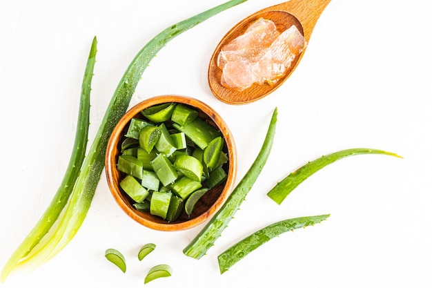 Fette di una pianta naturale di aloe vera in una ciotola di legno e pezzi di gel in un cucchiaio su sfondo bianco vista dall'alto foglie della pianta