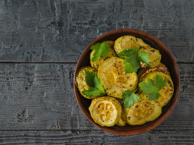 Fette di zucchine al forno in una ciotola di argilla su un tavolo di legno nero