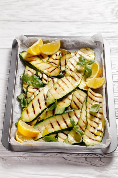 Fette di zucchine grigliate su una teglia con limone e foglie di basilico fresco, cucina italiana
