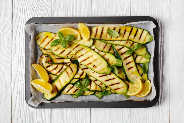 Fette di zucchine grigliate su una teglia con limone e foglie di basilico fresco, piatto, cucina italiana