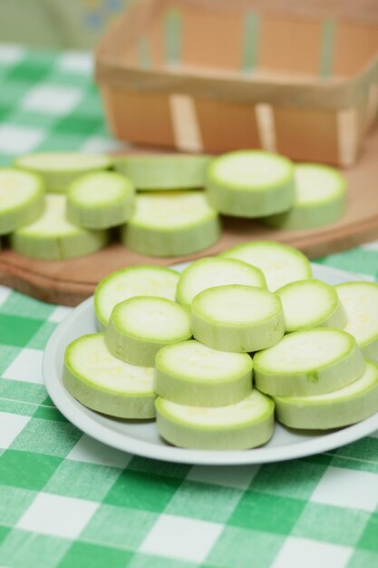 Fette di zucchine su un piatto bianco e una tavola di legno su una tovaglia verde Verdure sane Primo piano