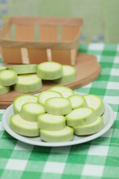 Fette di zucchine su un piatto bianco e una tavola di legno su una tovaglia verde Verdure sane Primo piano