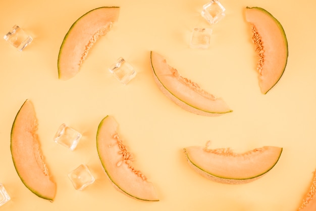 Fette fresche del cantalupo con i cubetti di ghiaccio su fondo beige