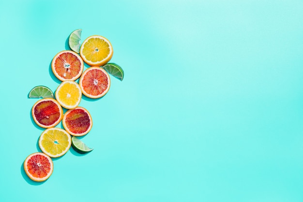 Fette luminose di agrumi, pompelmo, arancia rossa, limone, lime su sfondo turchese pastello. La minima frutta e il concetto di estate.