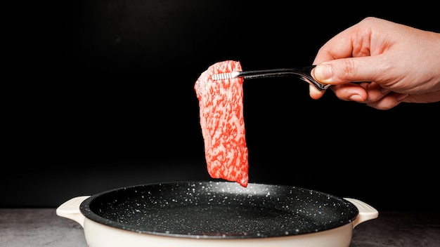 Fette Rare Premium Controfiletto Wagyu A5 con struttura ad alta marmorizzazione raccolta su una padella antiaderente rivestita di marmo da pinze per barbecue con mano su sfondo nero Servito per Yakiniku