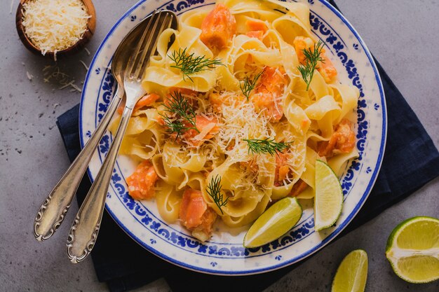 Fettuccine con salmone e parmigiano in salsa cremosa nel piatto di ceramica sulla vecchia superficie di cemento grigio. Vista dall'alto.