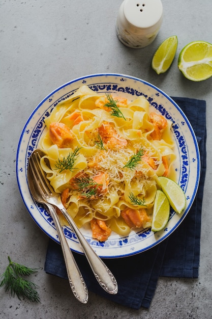 Fettuccine con salmone e parmigiano in salsa cremosa nel piatto di ceramica sulla vecchia superficie di cemento grigio