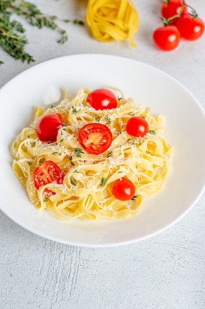 Fettuccine fatte in casa con pomodori, timo, parmigiano in un piatto bianco su una superficie leggera