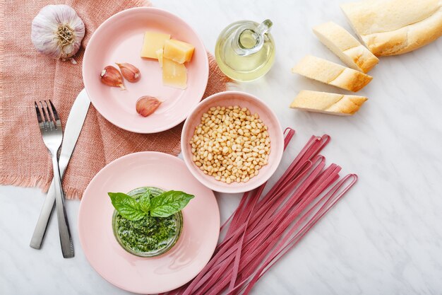 Fettuccine rosa crude e salsa al pesto con ingredienti in piatti rosa sul tavolo di marmo bianco