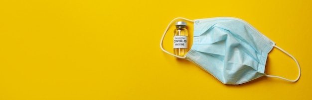 Fiala di vaccino Covid - 19 e maschera su sfondo giallo