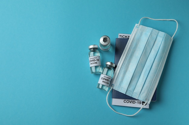 Fiale con vaccino COVID - 19, mascherina medica e passaporto sul tavolo blu