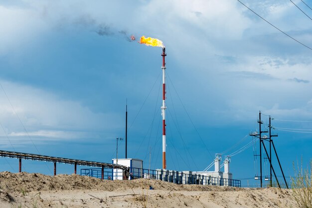 Fiammata di gas. Giacimento petrolifero con torcia sullo sfondo del cielo blu. Estrazione dell'olio. Concetto di petrolio.