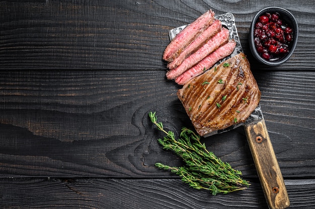 Fianco affettato o bistecca di carne di manzo bavette su una mannaia. Fondo in legno nero. Vista dall'alto. Copia spazio.